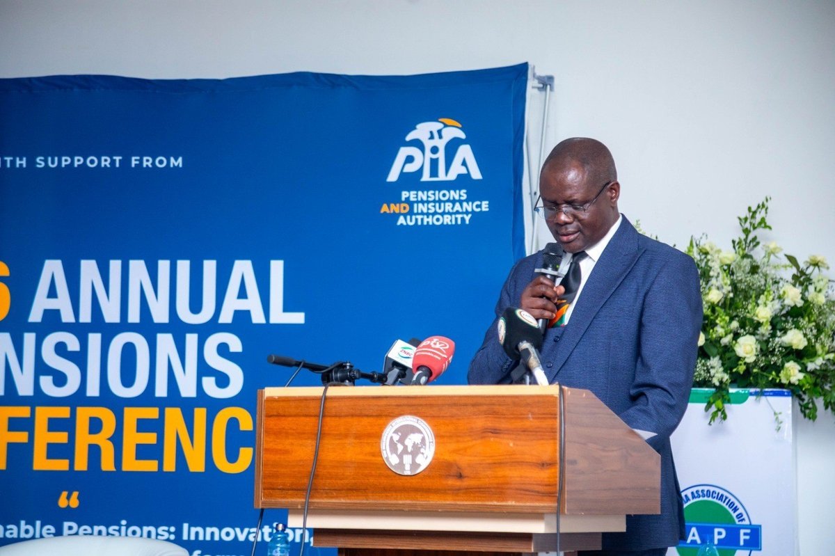 A speaker in a blue suit addresses the 2026 Annual Pensions Conference from a wooden podium with press microphones, in front of a blue banner carrying the Pensions and Insurance Authority logo.